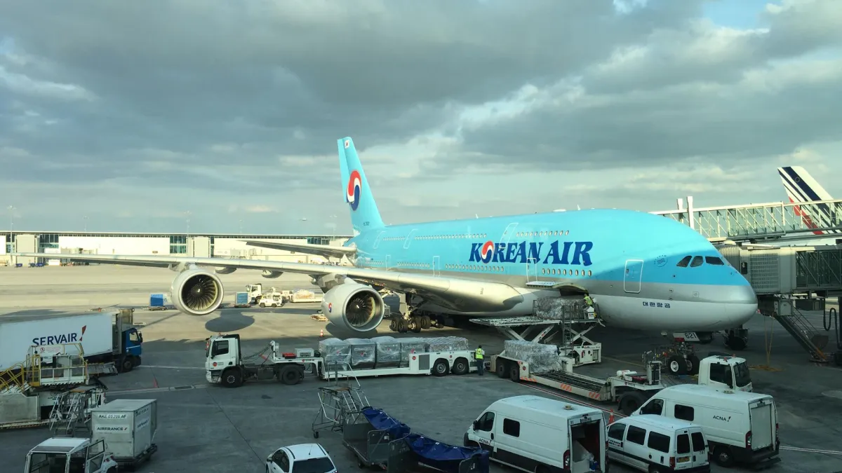 A Korean Air Airbus A380 in sky-blue livery at a Paris Charles de Gaulle stand, ground vehicles and cargo pallets alongside