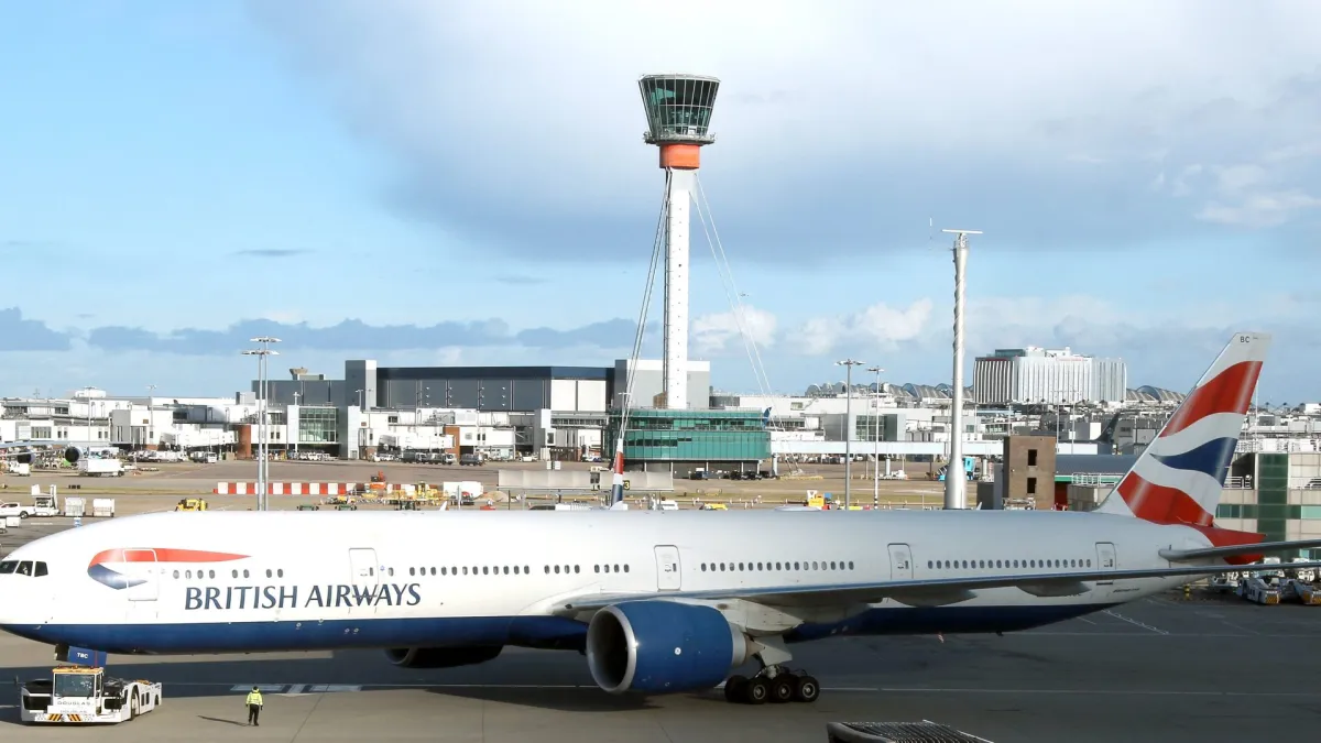 A British Airways Boeing 777-300ER on stand at London Heathrow, Union flag tail and the airport control tower behind it