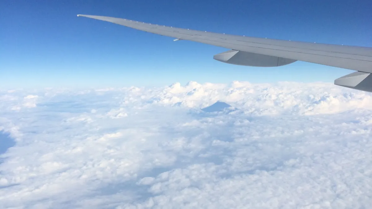 View from an aircraft window at cruise altitude: a grey wing tip against deep blue sky above a bright, unbroken cloud layer