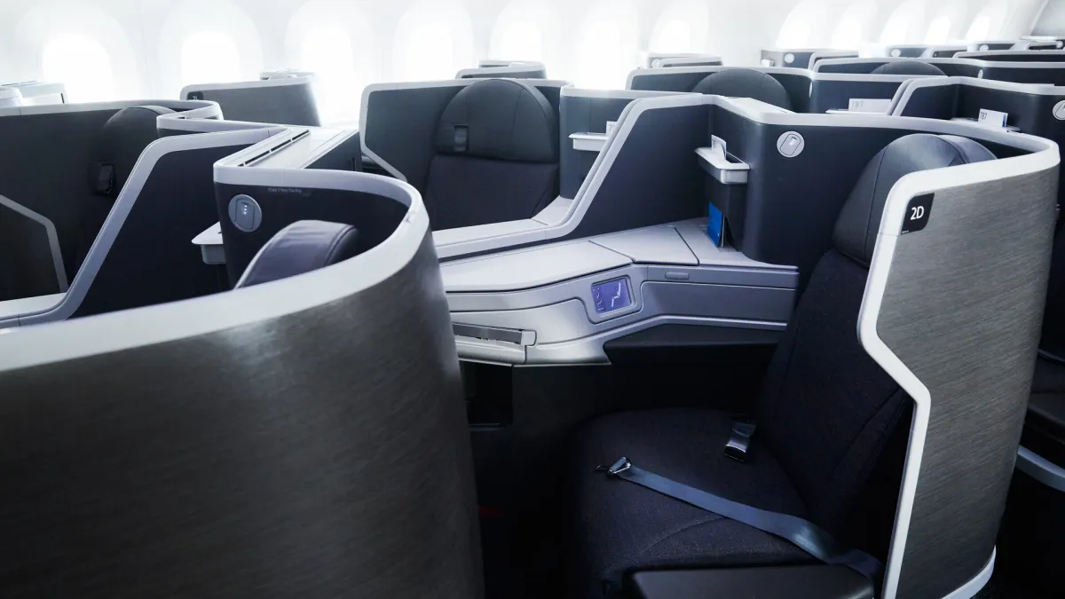 Fully flat business class pods in a widebody cabin, charcoal shells with white trim, photographed down an empty aisle